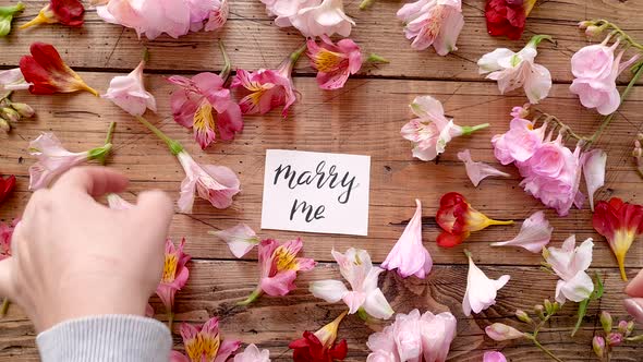 Put a flowers around a MARRY ME card on a wooden table top view