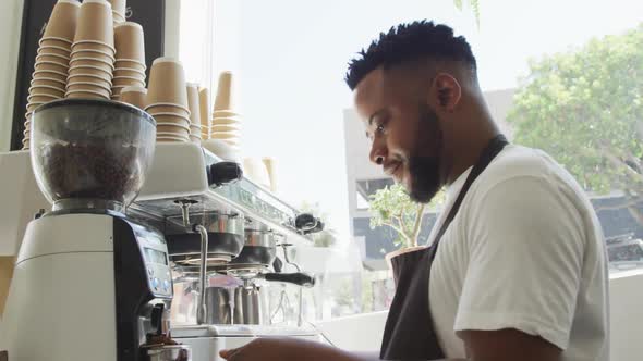 Happy african american male barista making coffee using coffe machine at cafe