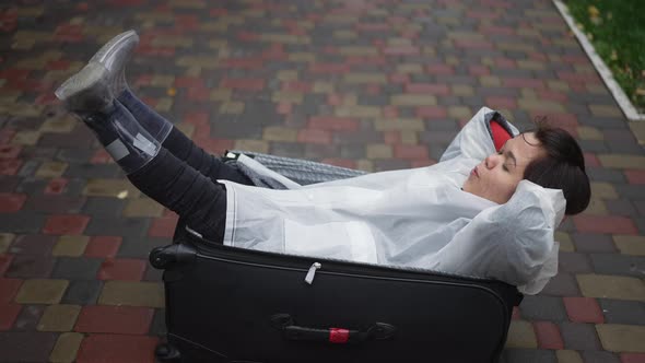 Joyful Carefree Little Woman Lying in Travel Bag Shaking Legs Smiling