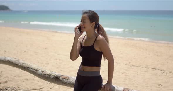 Cheerful Ethnic Sportswoman Speaking on Smartphone on Beach