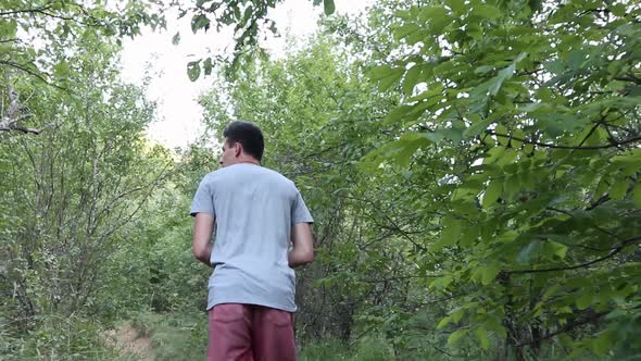 A man walks on a footpath in forest, daytime,  summer season. Young man filmed from behind while Wal