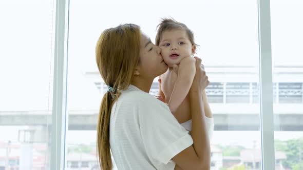 Happy young adult asian mom holding cute adorable infant child girl lifting up standing in bedroom