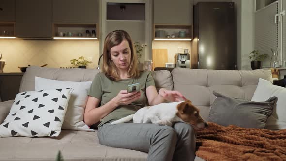 Woman Sitting on Sofa with Dog and Use Smartphone