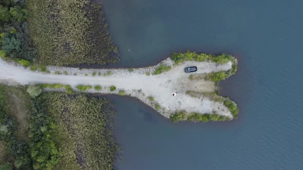 White sanded penisula in a lake with a picnicing coucle and a parked car from above - time for roman