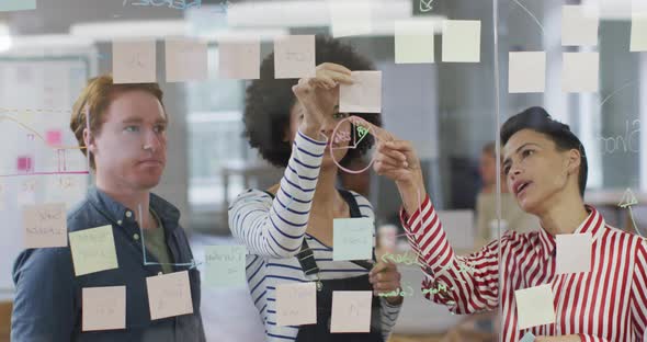 Diverse male and female business colleagues discussing by glass wall with memo notes