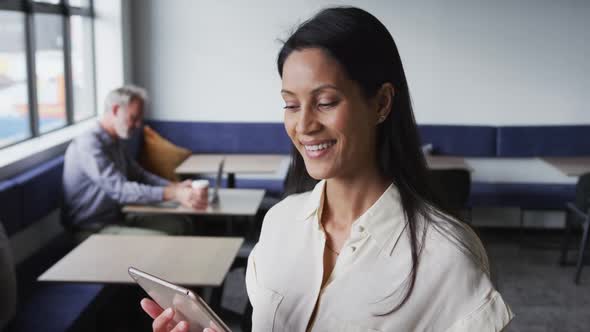 Portrait of mixed race businesswoman standing using digital tablet in office