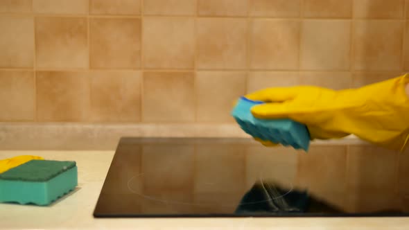 Woman Hand in Yellow Glove Carefully Cleans Induction Cooker with Blue Cleaning Sponge   Close Up