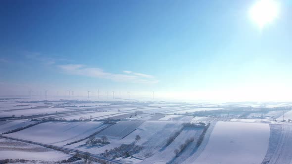 Icy Cold Winter At Vast Agricultural Land With Wind Turbines At Background. Aerial Wide Shot