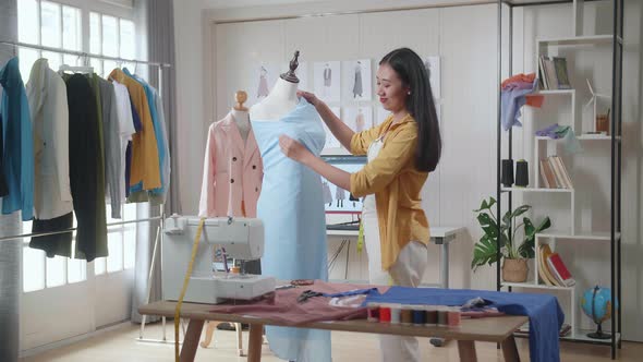 Asian Female Designer Using Needle Wearing Fabric On A Mannequin While Designing Clothes