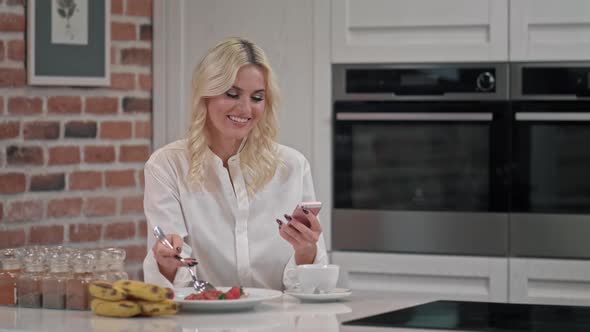 Portrait of Blond Woman Texting Message on Smartphone at Kitchen Smiles and Laughs