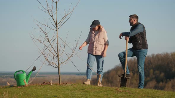 Couple of Volunteers Discussing Something While Standing Next to a Planted Tree