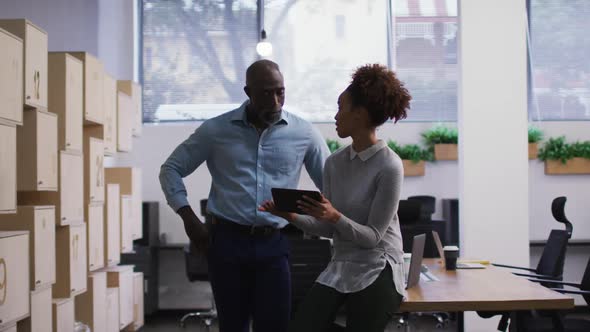 Diverse male and female business colleagues talking and using digital tablet in office