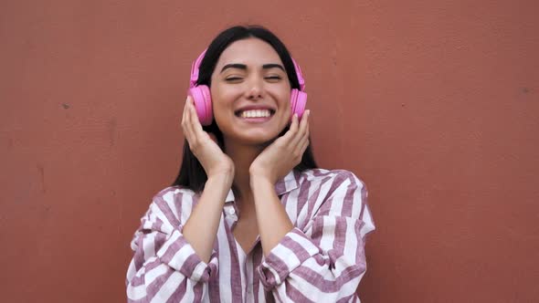 Happy young Latin woman having fun listening music with wireless headphones outdoor