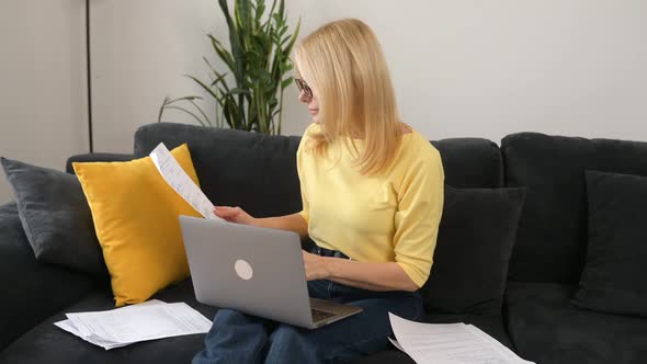 Confident 50s Middleage Female Employee Using Laptop for Remote Work Sitting on the Sofa at Home