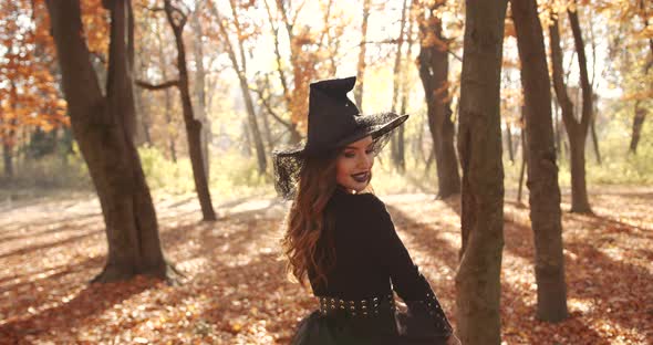 Attractive Woman in a Special Dress and Hat Looks Like a Witch in the Autumn Forest