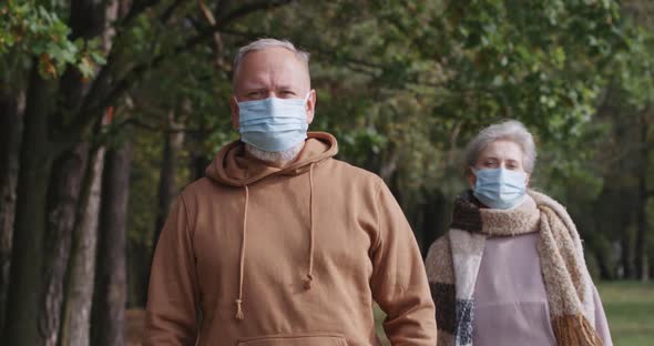 Elderly Couple on Walk in a Forest Park, Autumn Day, Gray-haired Man and a Woman in Medical Masks