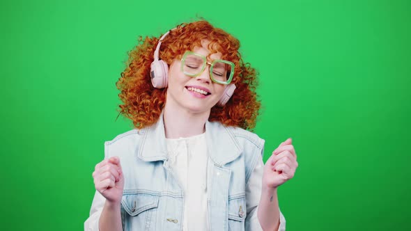 Playful Redhead Curly Lady Listening to Music in Wireless Headphones and Dancing Green Chroma Key