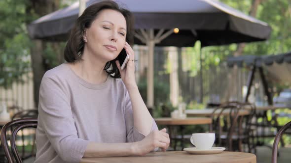 Old Woman Talking on Phone, Sitting in Outdoor Cafe