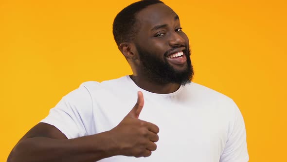 Smiling Afro-American Male Showing Thumbs Up and Winking, Yellow Background