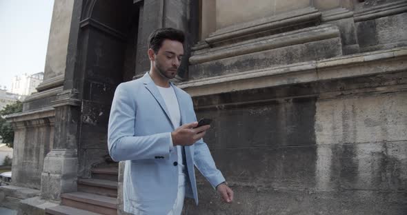 Young Man Reads An SMS On The Phone While Walking Around The City