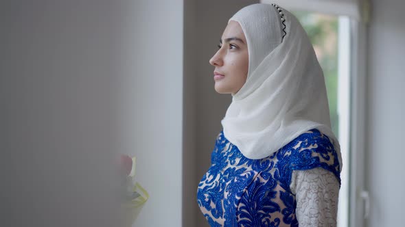 Confident Serious Middle Eastern Bride in Hijab and Wedding Dress Looking Out the Window Turning to