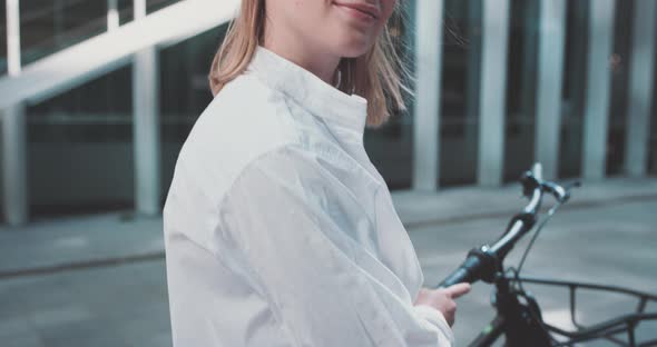 Young blond business woman smiles looking at the camera standing next to a bicycle