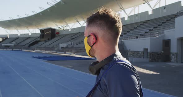Caucasian male athlete wearing face mask and headphones on sunny day