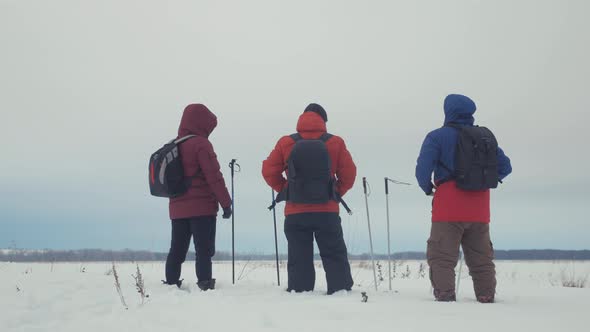 Back View of Three Tourist Hikers with Trekking Poles, a Backpack and Snowshoes. Happy Hikers Group