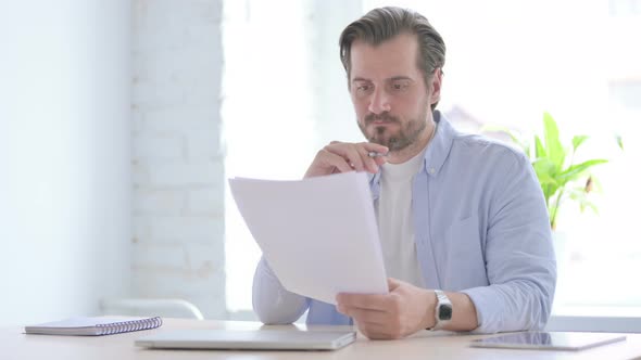 Young Man Reading Reports While Sitting in Office