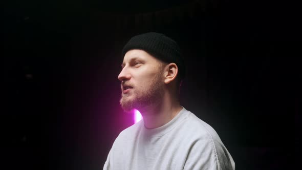 Side View of a Young Man in a Black Cap Talking and Giving Interview Against Black Background