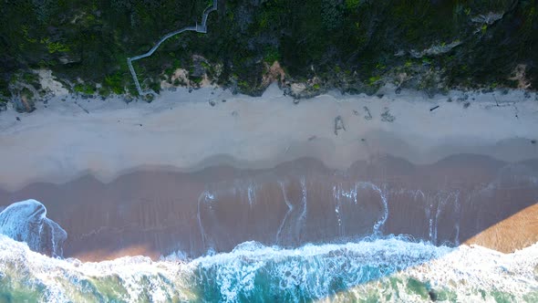 Gentle waves runs onto pristine white sand beach, aerial top-down