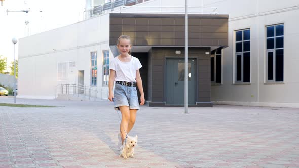 Teenage Girl Walks with Puppy on Leash on Yard Pavement