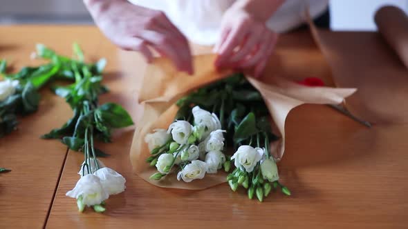 view as female wrapping a white roses in a bouquet on a table