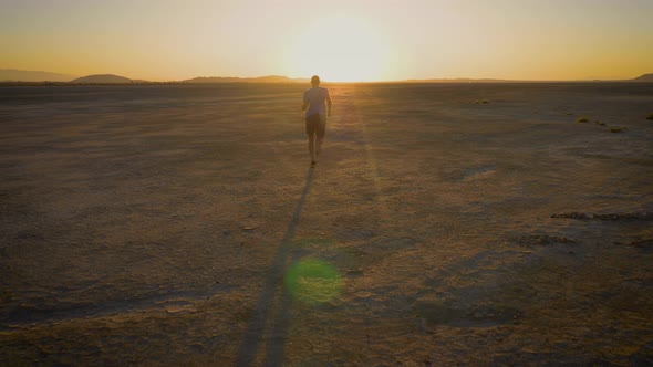 Athletic man working out with battle ropes on a dry lake at sunset