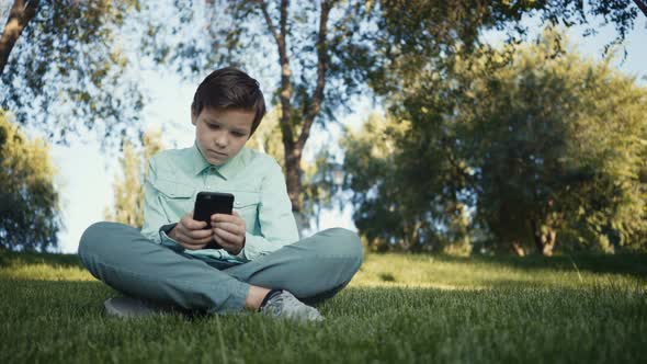 Teenager Playing Video Games on His Smartphone Outdoors