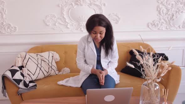 Female Black Clinician in White Gown Using Laptop for Remote Patient Consultation in Hospital