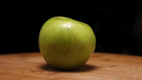 A green ripe apple on a wooden background. The camera flies around