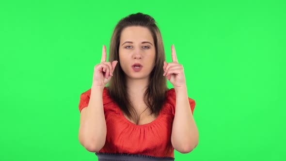 Portrait of Cute Girl Pointing Fingers Up for Something with Copy Space.. Green Screen