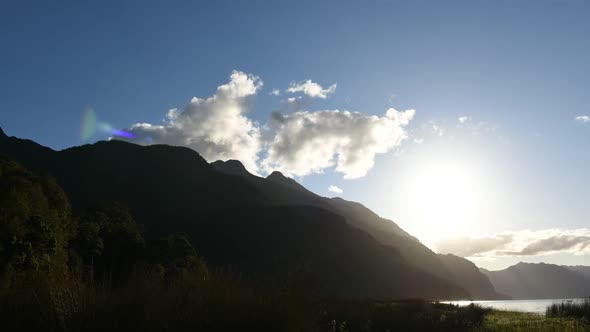 Time lapse view of mountains backed by sunlight and fluffy clouds