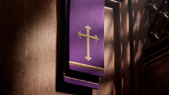 Purple stole with cross lightened by rays of light falling into a confessional.