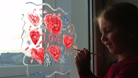 Little girl holds paintbrush in hand draws red heart on window Valentine's day love home family art