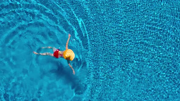 View From the Top As a Woman in a Red Swimsuit and a Big Yellow Hat Swims in the Pool