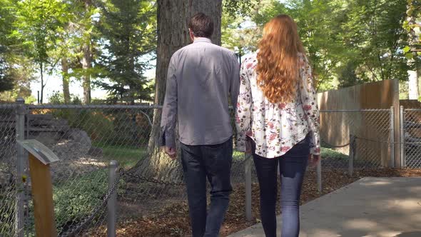 Couple holding hands walking on sidewalk through aviary