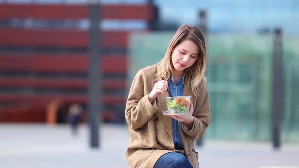 Woman sits on some bench on street and eating dinner
