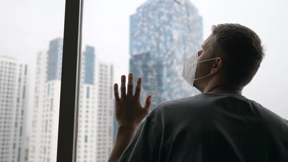 An Adult Caucasian Man in Face Mask Looking Through the Window of a Skyscraper