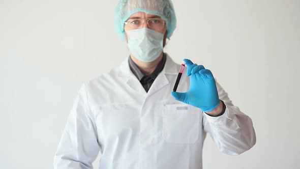 A Doctor in a White Coat and Protective Mask Shows a Sample of Blood in a Test Tube and Keeps Thumb