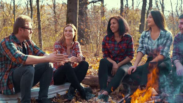 Multiracial group of hikers storytelling by campfire in autumn forest
