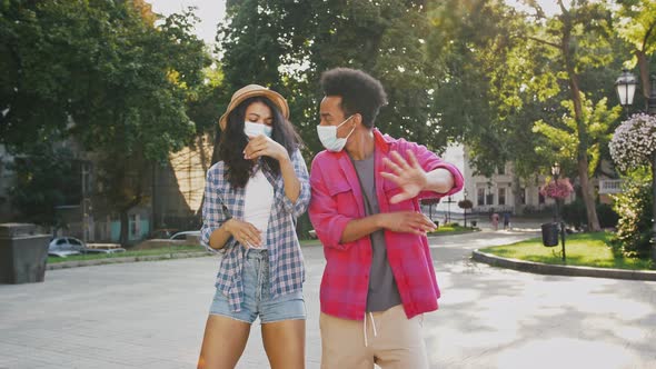 Darkskinned Male and Female in Protective Masks are Dancing at City Park