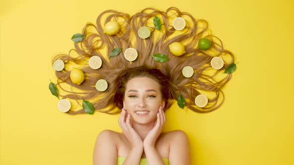 beautiful girl lying with citrus fruits on long hair, concept care and beauty,head with lemons