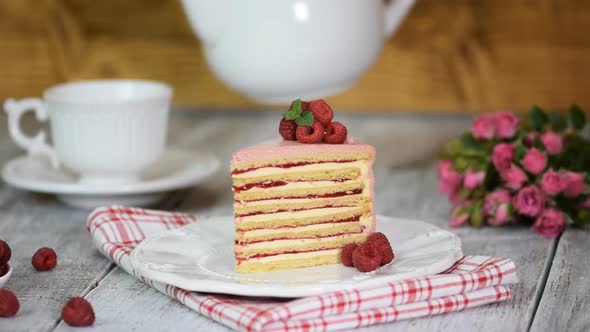 Portion a layered creamy fruit cake with a cup of tea. Pours tea into cup.